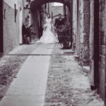 Sposi camminano verso l'obiettivo in un caruggio ligure ad arco, bianco e nero | Fabio Zenoardo