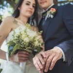 Mani degli sposi mostrano le fedi nuziali dorate verso l'obiettivo con bouquet verde | Fabio Zenoardo