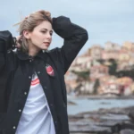 Fotografo street Liguria - modella giacca nera t-shirt Evangelion lungomare vento