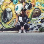 Fotografo street Liguria - modella look urban seduta murale graffiti colorato