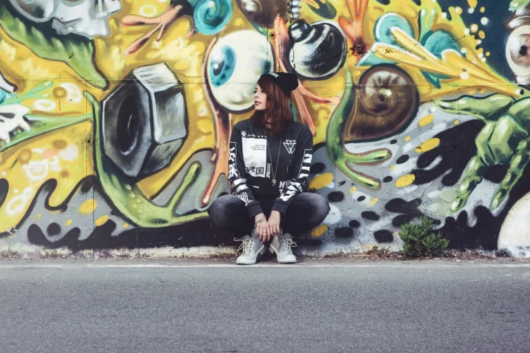 Fotografo street Liguria - modella look urban seduta murale graffiti colorato