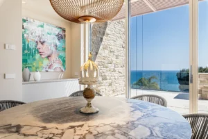 Zona pranzo con tavolo ovale in marmo, lampada in rattan, opera d arte contemporanea e vista mare laterale