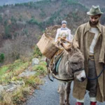 Uomo e donna in abiti tradizionali con un asino lungo una strada di montagna a Mendatica, nel Parco delle Alpi Liguri
