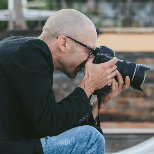 Fabio Zenoardo fotografo professionista di Imperia che scatta con reflex, occhiali da sole e giacca nera